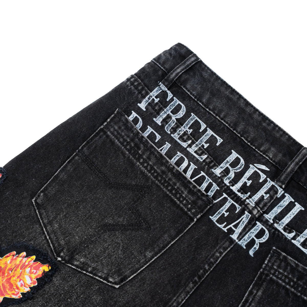 Close-up of the back waistband of black denim jeans featuring a large silver graphic that reads 'FREE REFILLS READYWEAR' and a colorful embroidered patch on the lower left.
