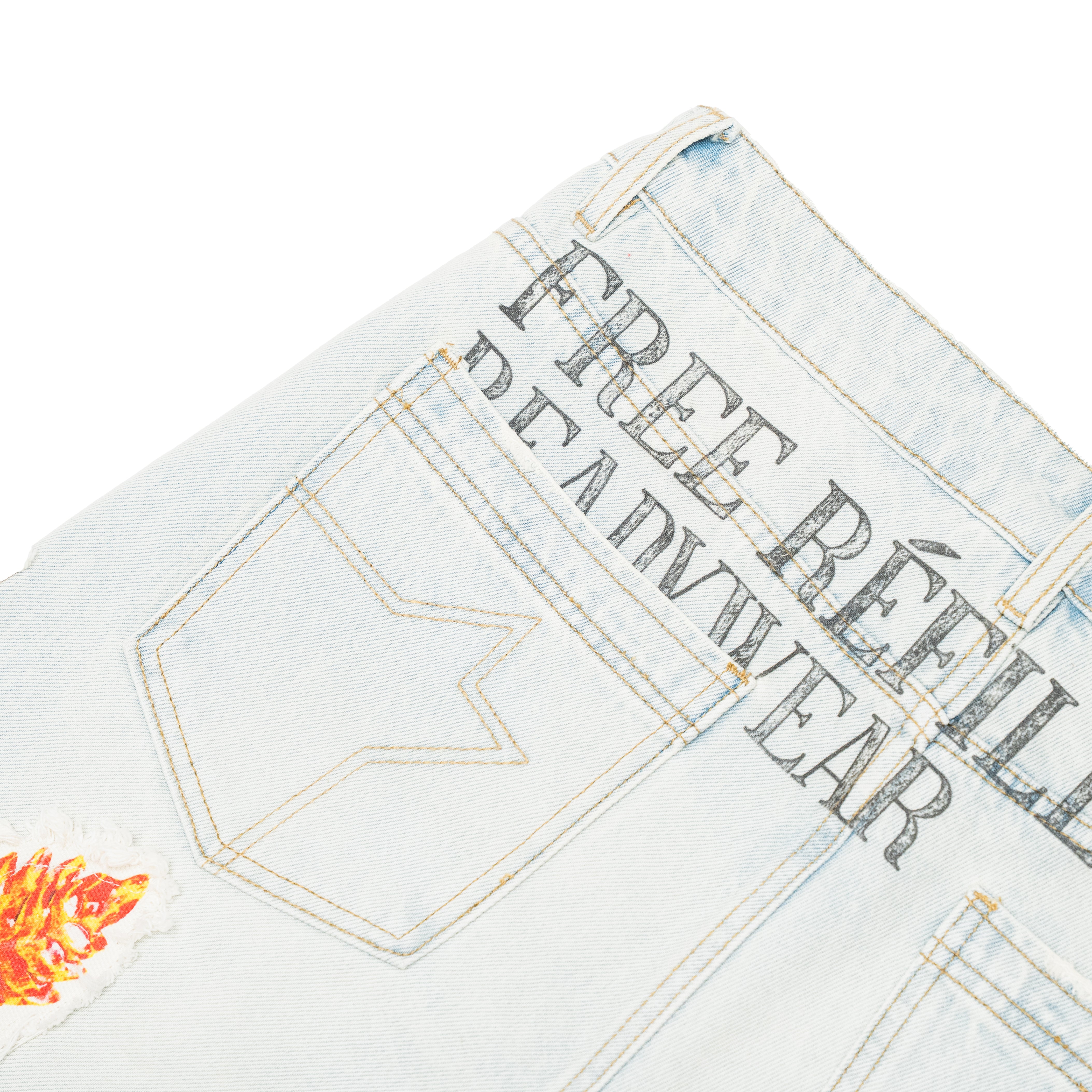Close-up of a light-wash denim garment, likely jeans or a jacket, showing the back pocket area with decorative stitching, large dark text reading 'FREE REFILLS READYWEAR', and a small orange flame patch near the lower left corner.