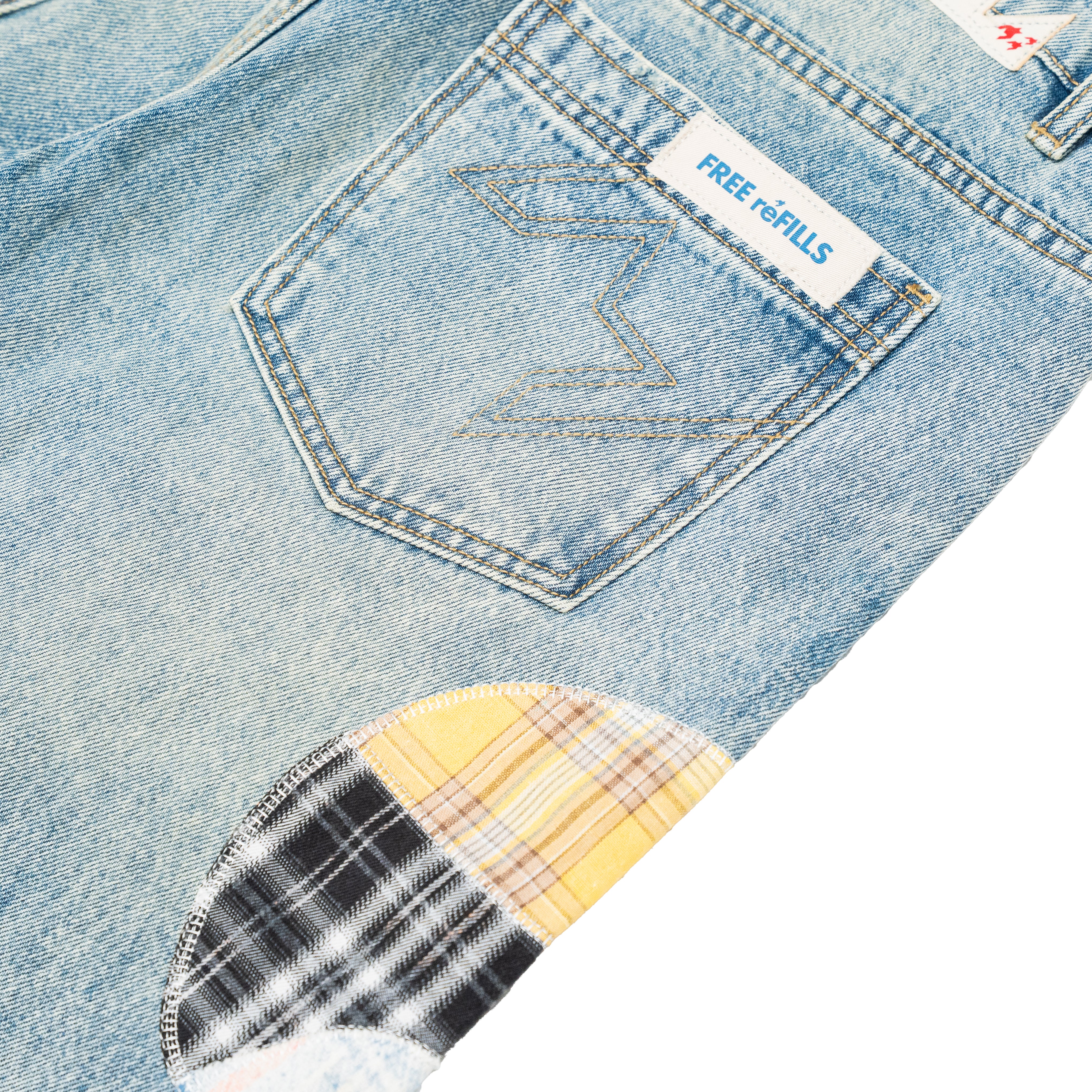 Close-up of light blue denim jeans showing the back pocket with a white 'FREE REFILLS' label, contrast stitching, and a plaid patch pocket detail.