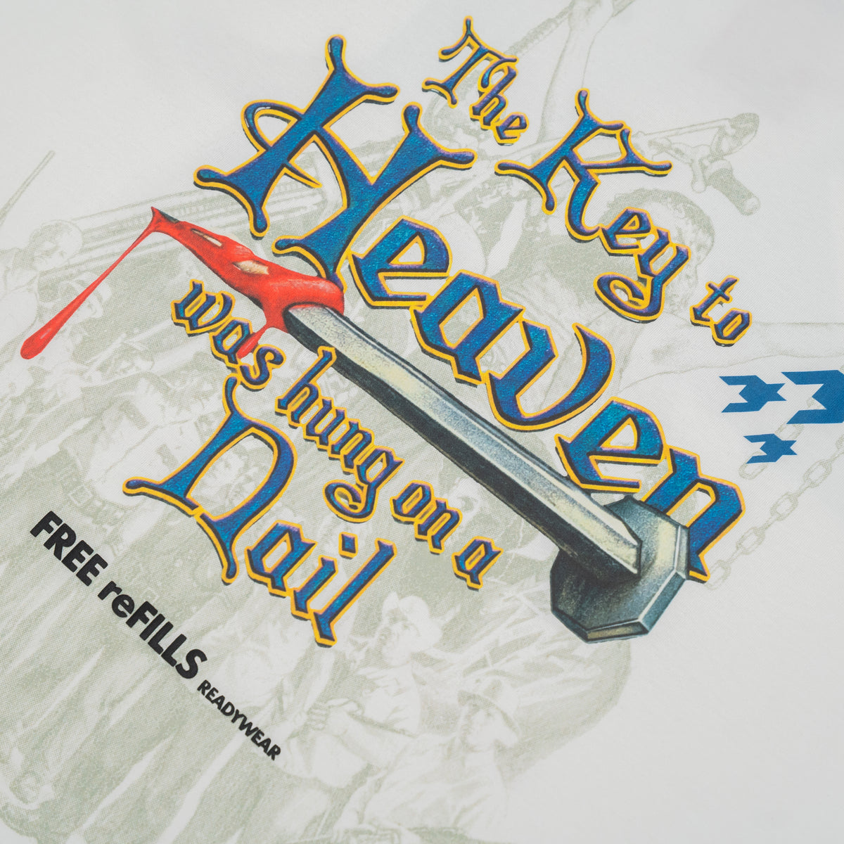 A close-up of a graphic print on a white t-shirt. The design features the text 'The Key to Heaven was hung on a Nail' in a stylized blue and gold font, accompanied by a silver nail illustration, a red cross, and a faint sepia-toned illustration in the background.