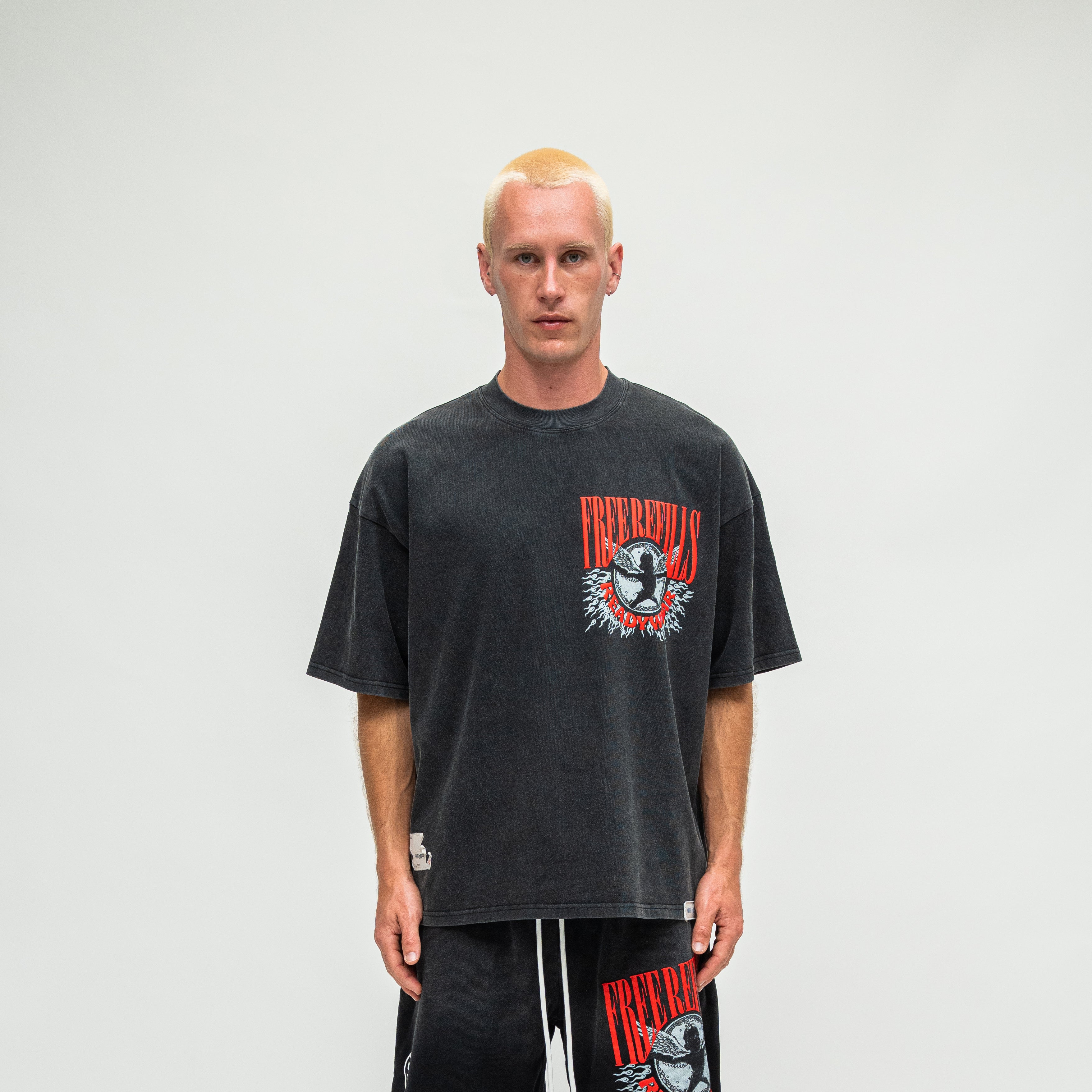 A man wearing a faded black graphic t-shirt and matching sweatpants with a red and white 'Nirvana' logo, standing against a light gray studio background.