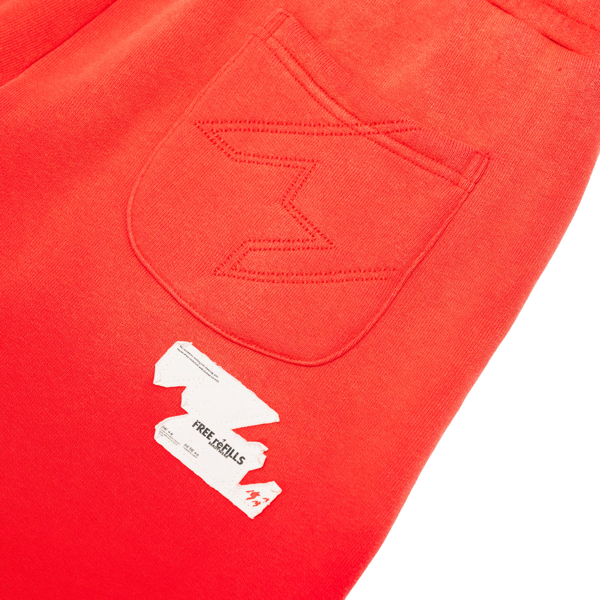 Close-up of bright red sweatpants showing a stitched back pocket and a white paper tag with the brand name Free REFILLS.