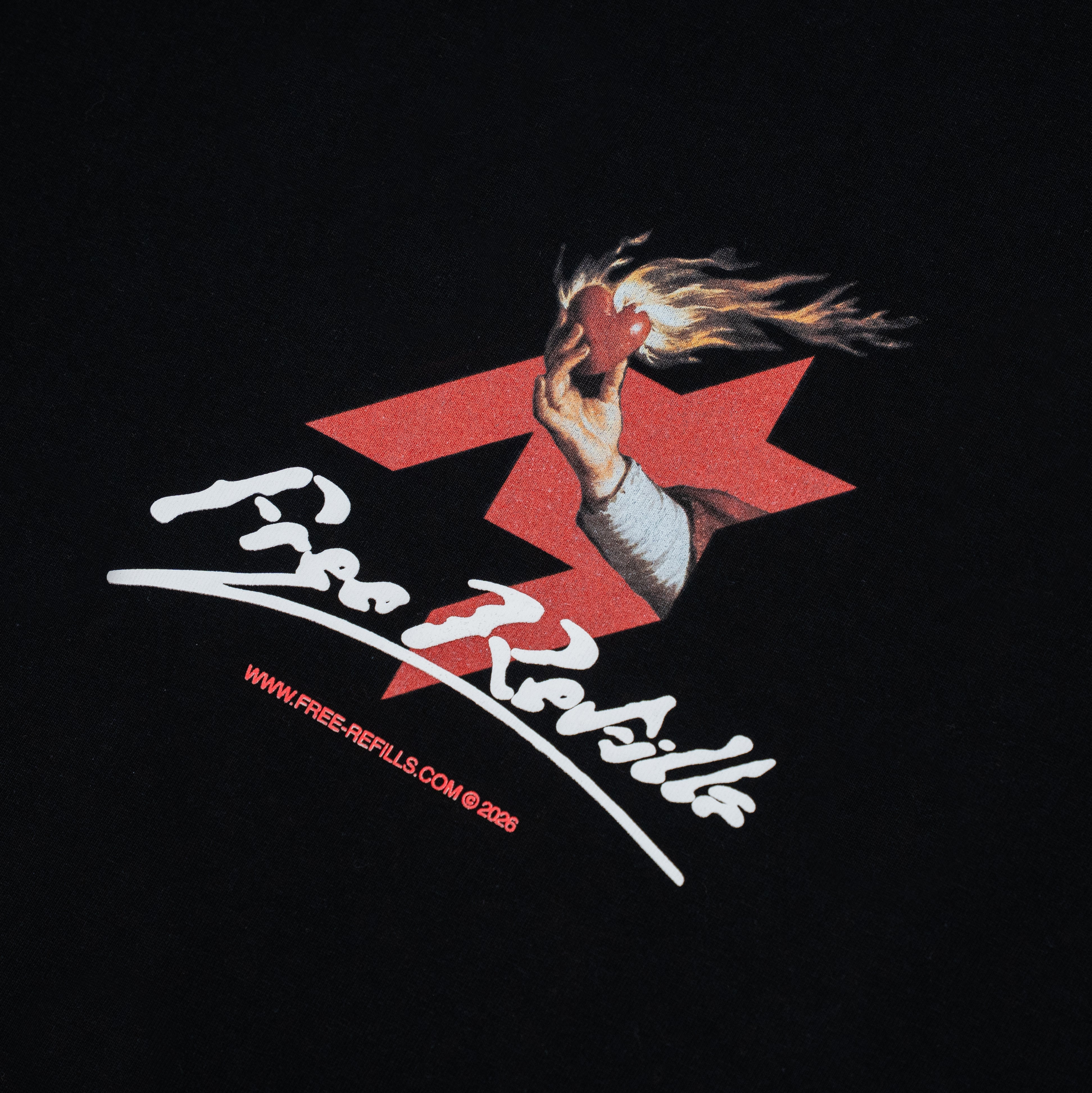 A close-up of a black garment featuring a graphic print with a hand holding a burning red heart in front of a red star, with the text 'Free Refills' in white script and smaller red website text below.