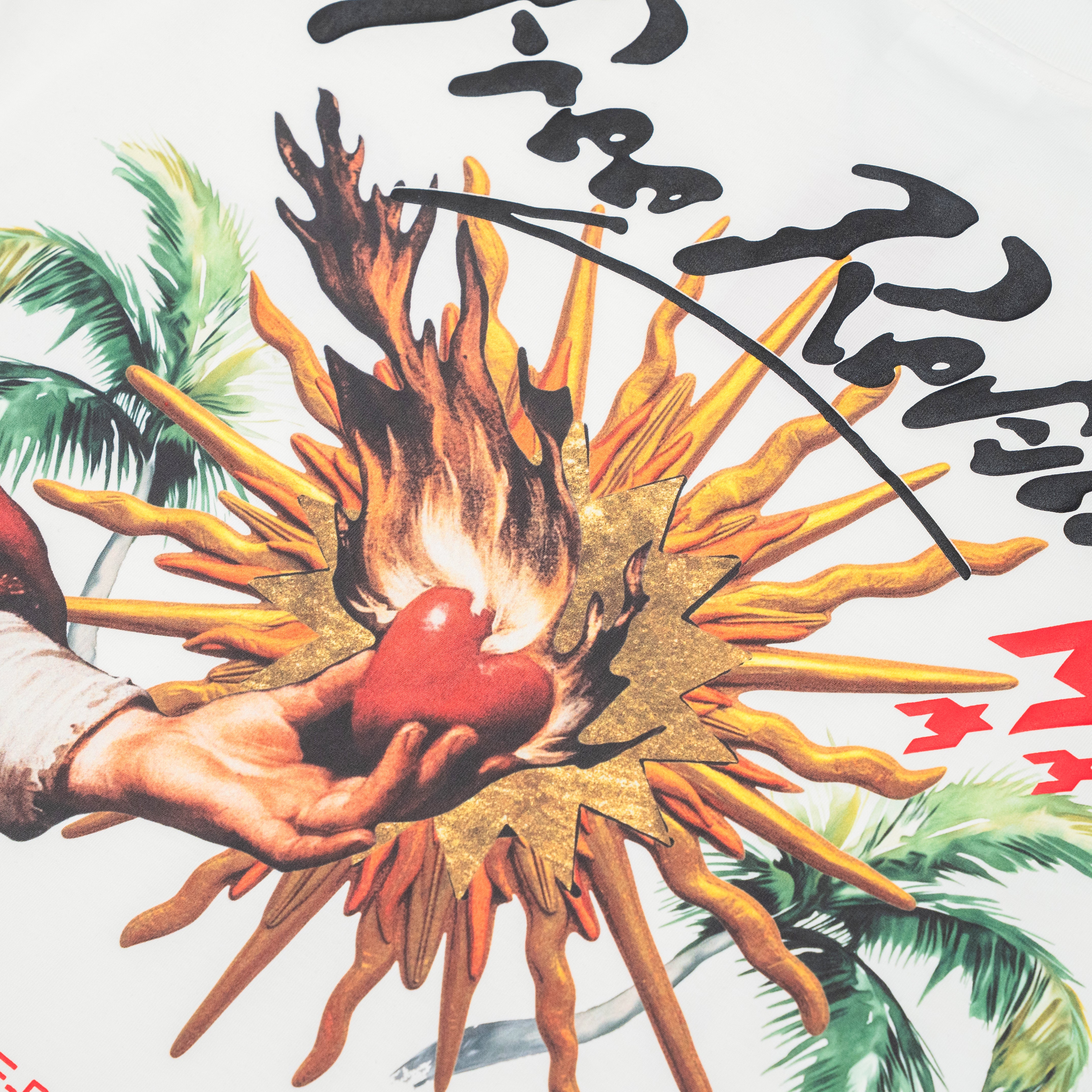 Close-up of a graphic print featuring a hand holding a red heart-like shape in front of orange and yellow flames, with green palm leaves and black script on a white background.