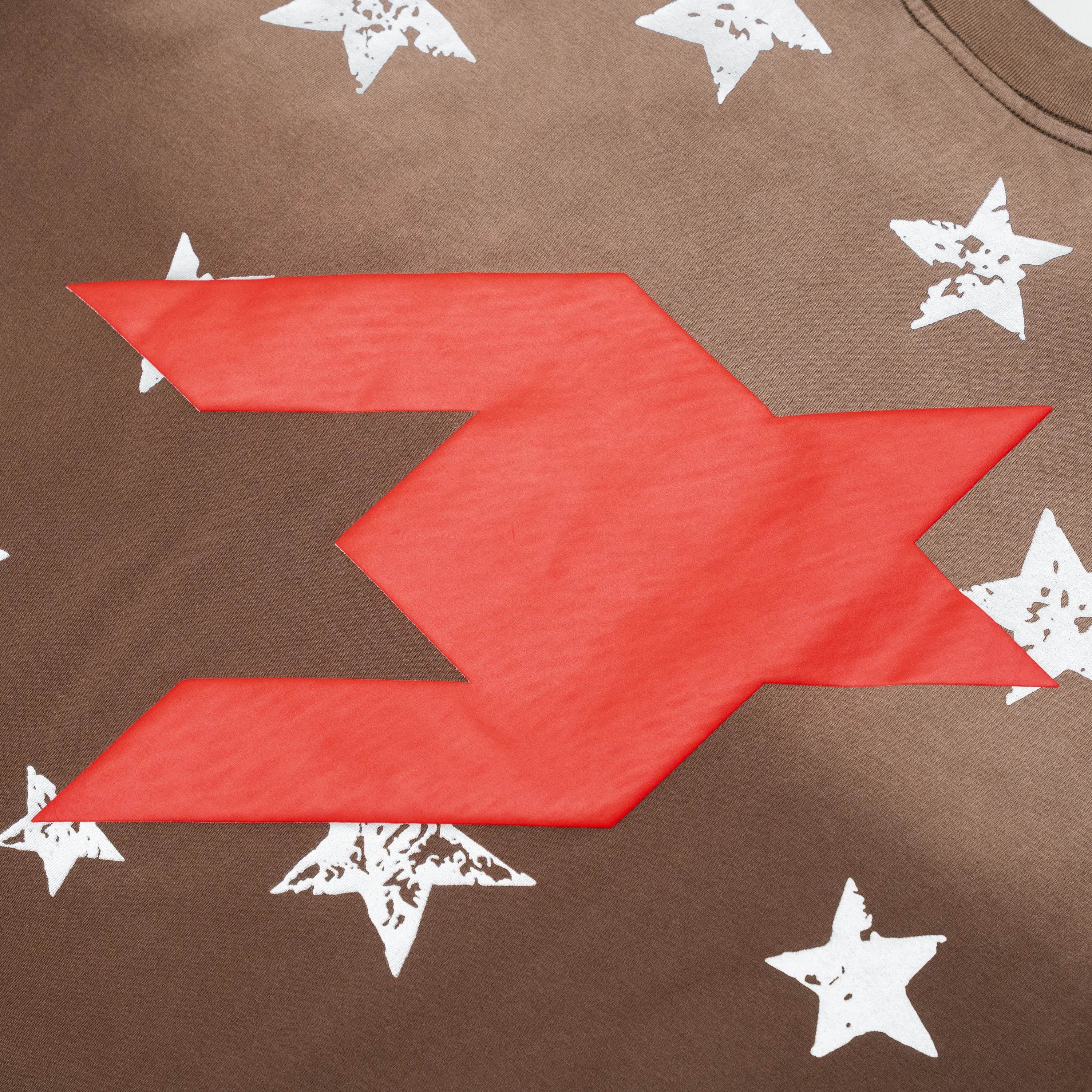 Close-up of a brown garment featuring a large red geometric logo patch and distressed white star prints.