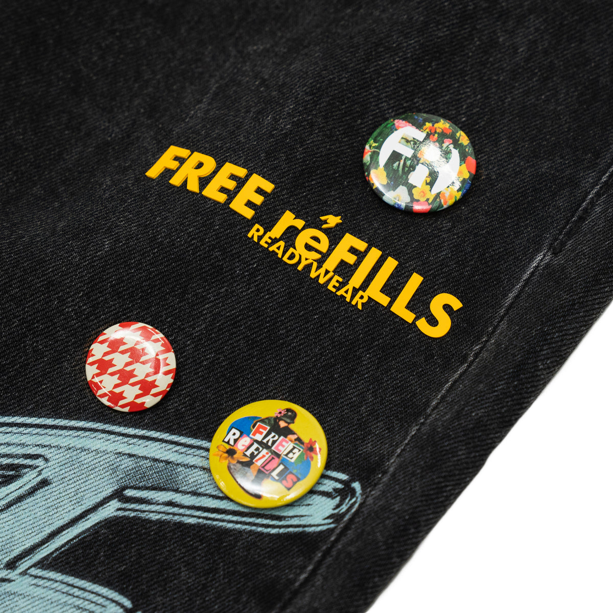 The Powder Room Jeans – Black – Close-up of yellow FREE ReFILLS lettering and colorful decorative pins