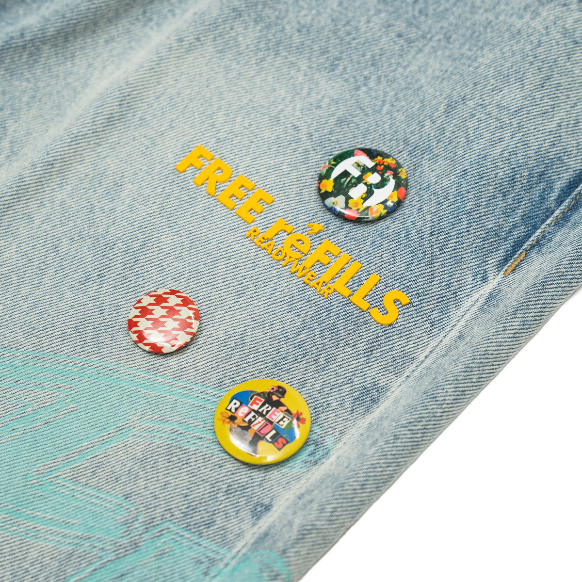 The Powder Room Jeans – Blue – Close-up of yellow FREE ReFILLS lettering and colorful decorative pins