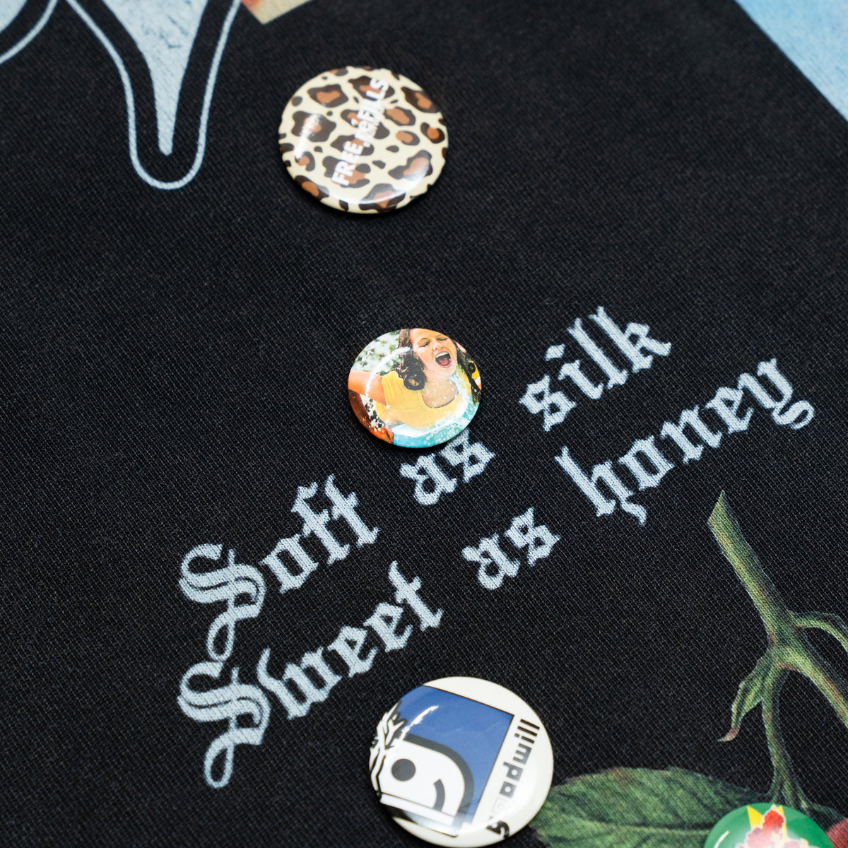 The Powder Room Tee – Black – Close-up of decorative pins and Soft as silk Sweet as honey lettering