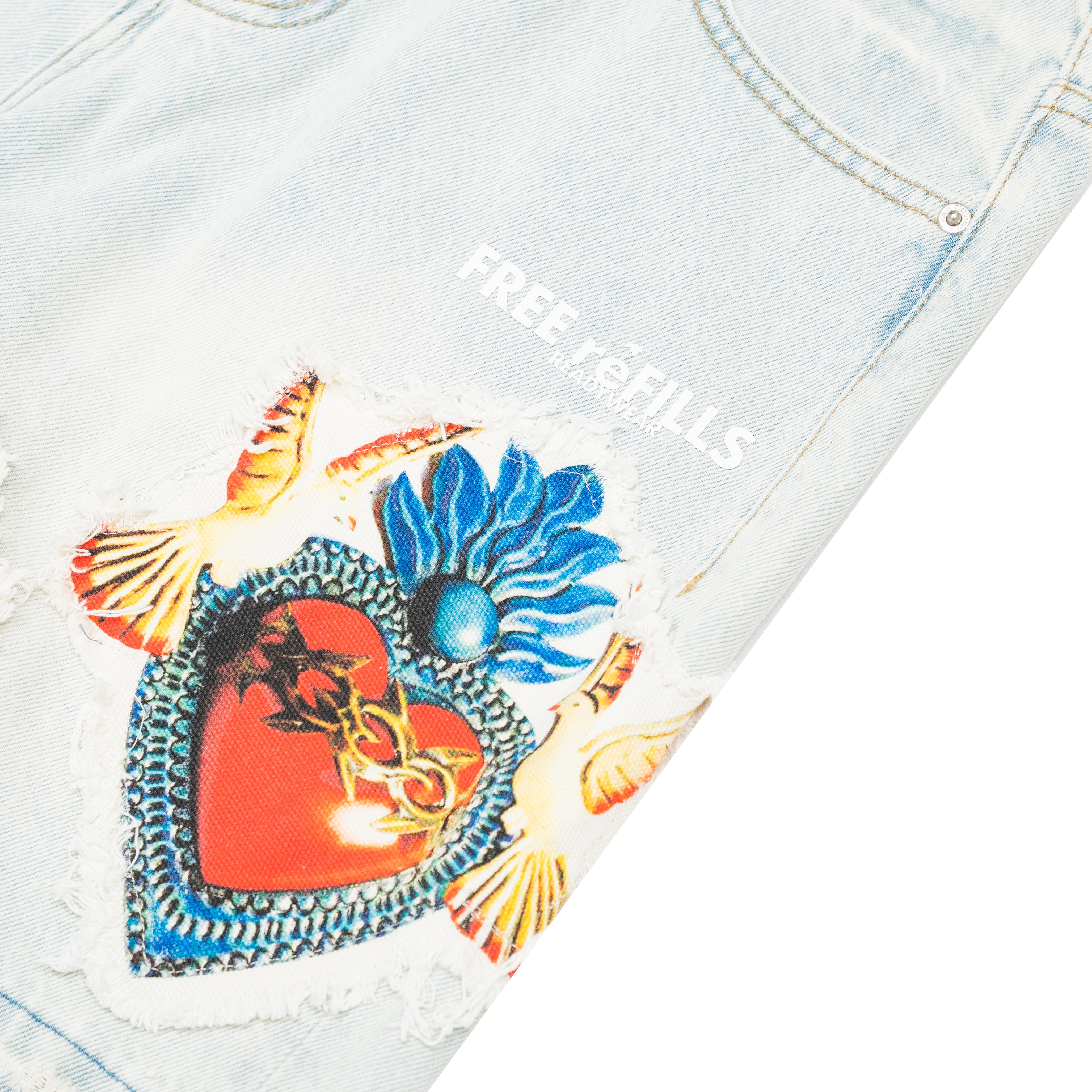 Close-up of light-wash denim jeans with a distressed patch featuring a red heart, blue flower, and gold chain details, plus white 'FREE REFILLS' text on the fabric.