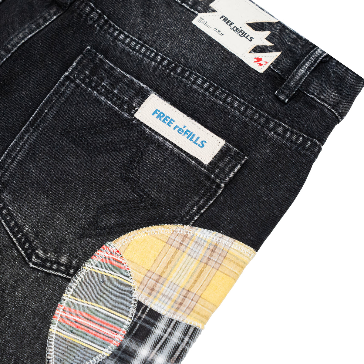 Close-up of a pair of black denim jeans showing the back pocket with a white 'FREE refILLS' label, a yellow plaid patch pocket, and a striped patch pocket on a white background.