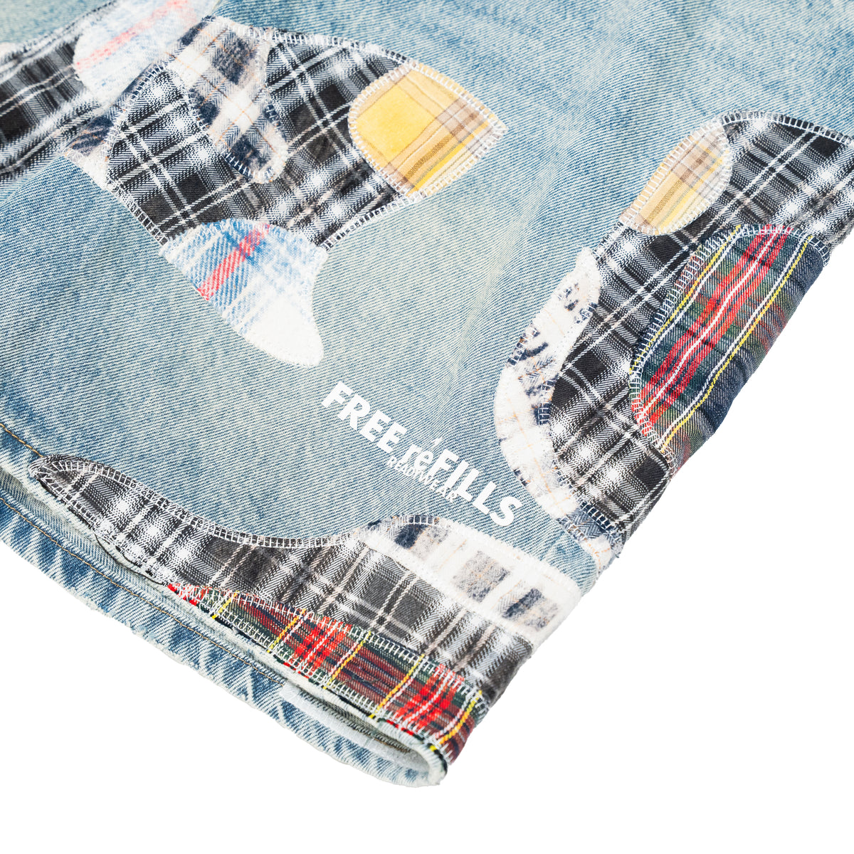 Close-up of a light blue denim garment with large patchwork plaid patches in black, white, red, yellow, and blue, plus the visible text 'FREE  REFILLS' on a white background.