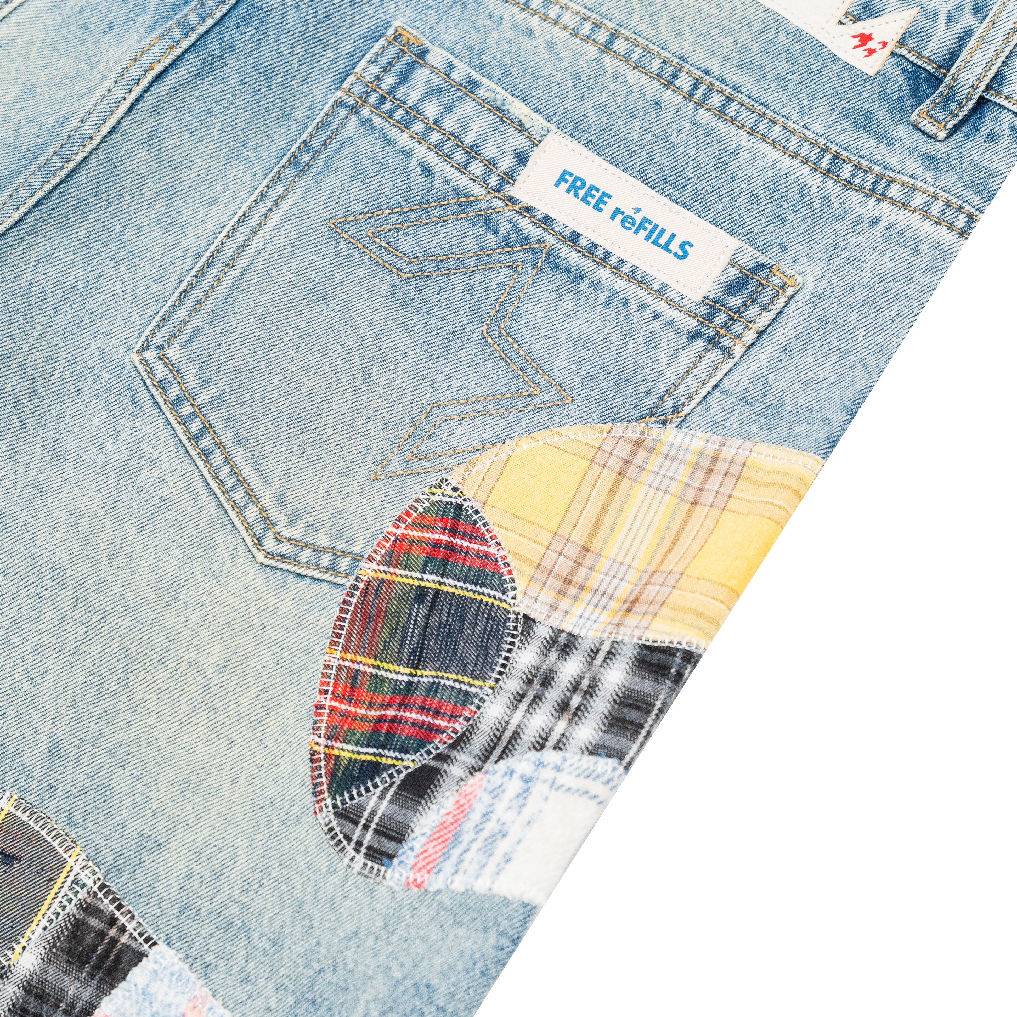 Close-up of a light blue denim pair with a decorative patchwork applique on the pocket, featuring a yellow plaid section and a red/black plaid section. A white brand label reading 'FREE REFILLS' is visible on the pocket.