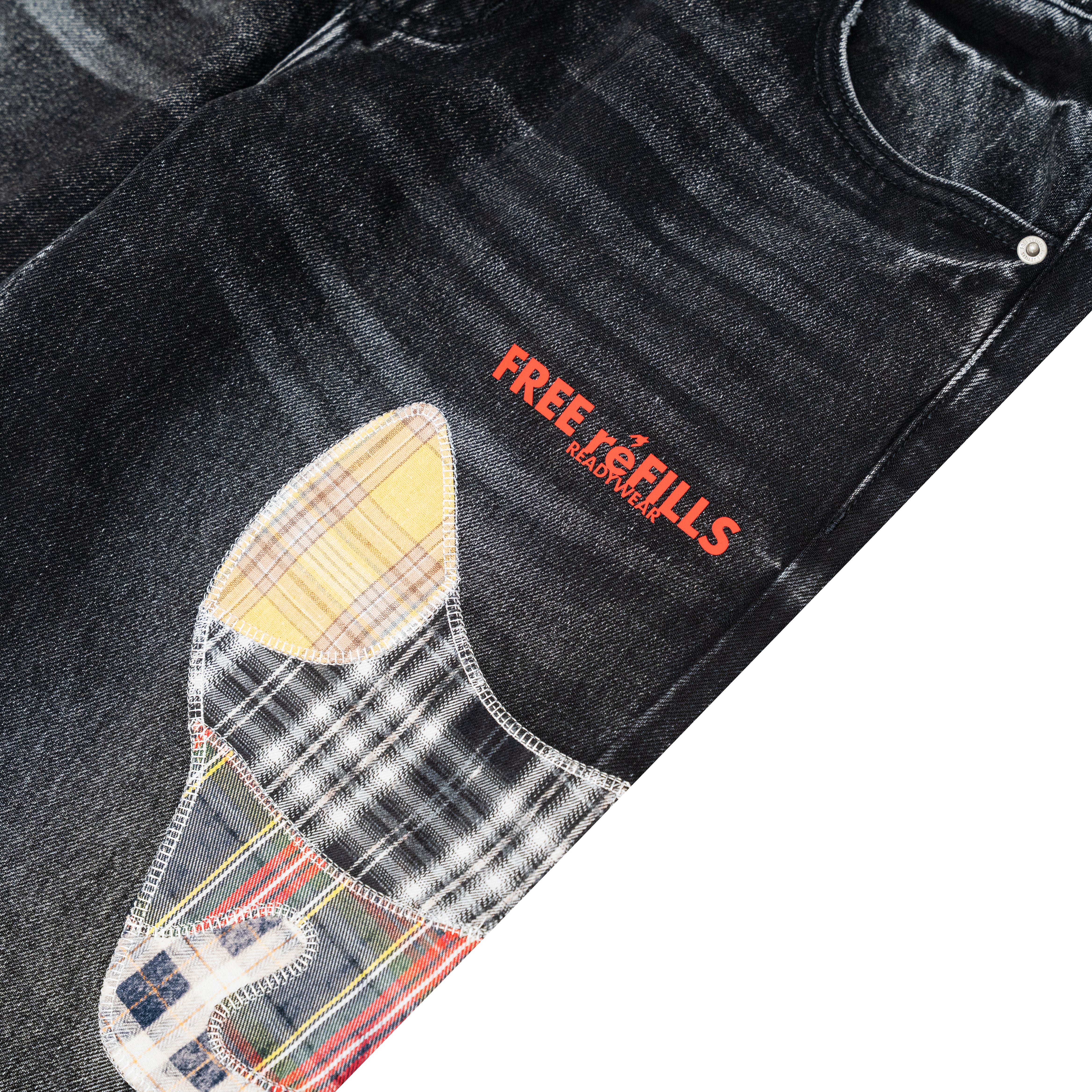 Close-up of a black denim jacket or denim garment with a large multicolor plaid patch on the front pocket and red embroidered text reading 'FREE REFILLS' on the thigh, shown against a white background.