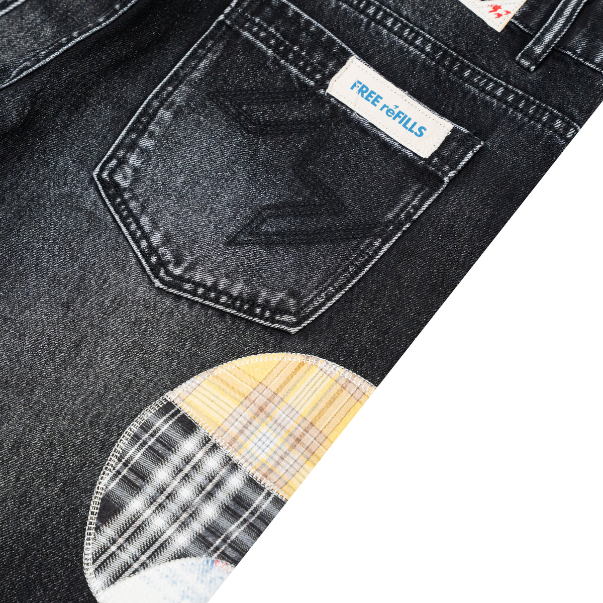 Close-up of dark washed denim jeans showing the back pocket with a visible FREE REFILLS label and a plaid patch detail near the lower left.