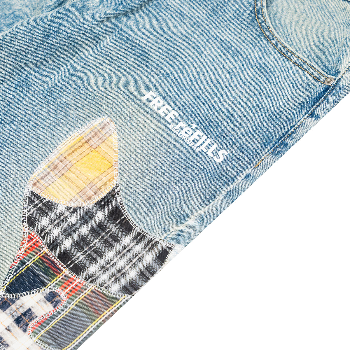 Close-up of light blue denim jeans with a large multicolor patchwork applique on the leg and white 'FREE REFILLS' text printed on the thigh.