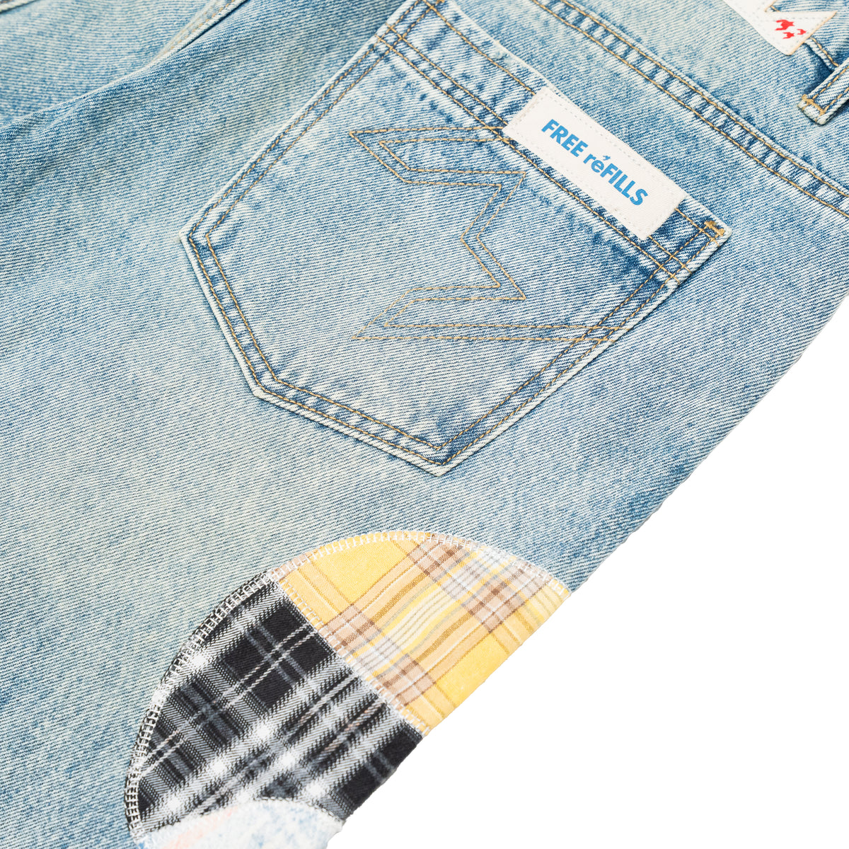 Close-up of light blue denim jeans showing the back pocket with a white 'FREE REFILLS' label, contrast stitching, and a plaid patch pocket detail.
