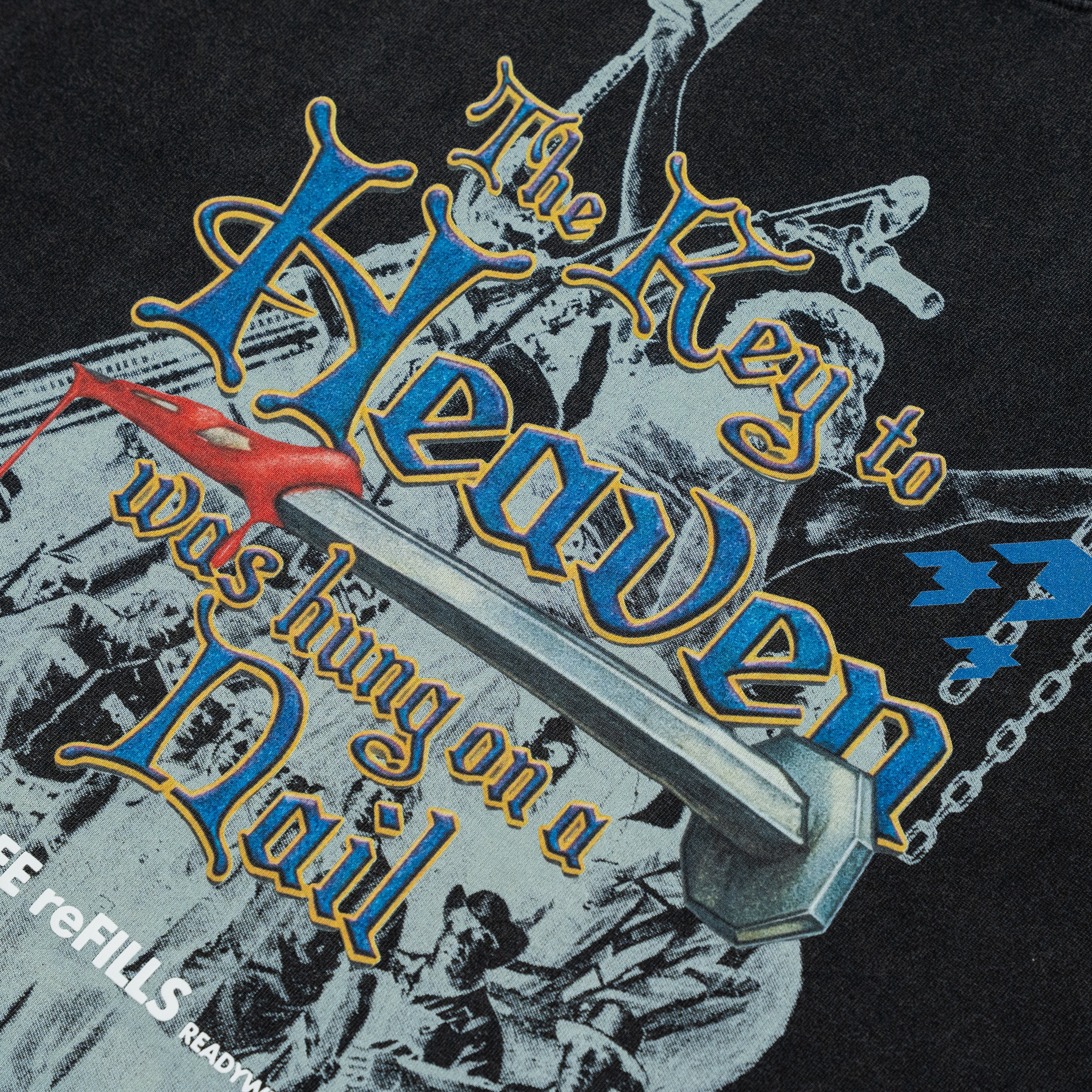 Close-up of a graphic print featuring the words 'The Key to Heaven was Hanging on a Nail' in stylized blue and gold lettering over a black background with grayscale imagery and a small red bird.