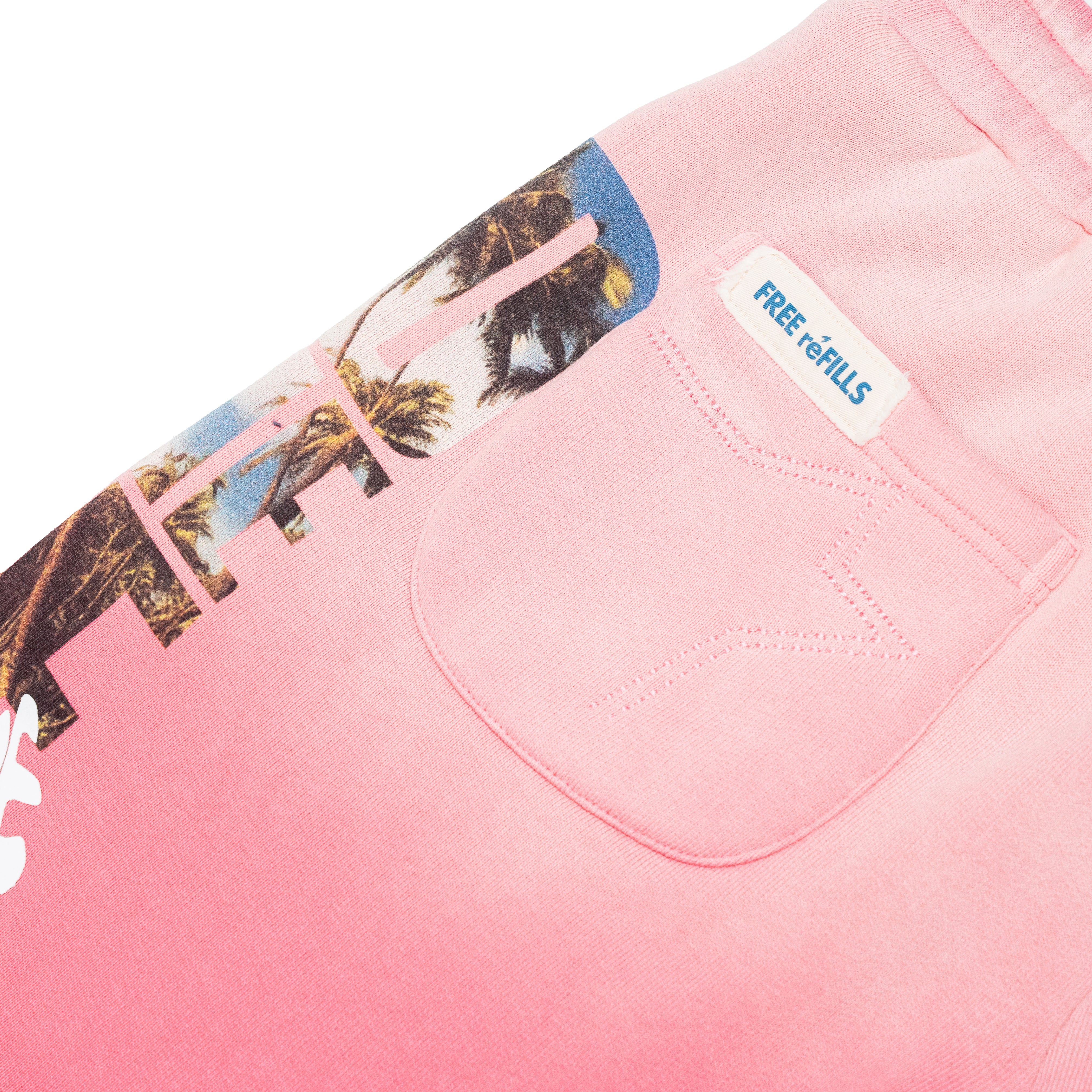 Close-up of a pink garment showing a front pocket with a white stitched star detail and a sewn-on label reading FREE-refILLS. A tropical palm tree graphic is partially visible along the left side.