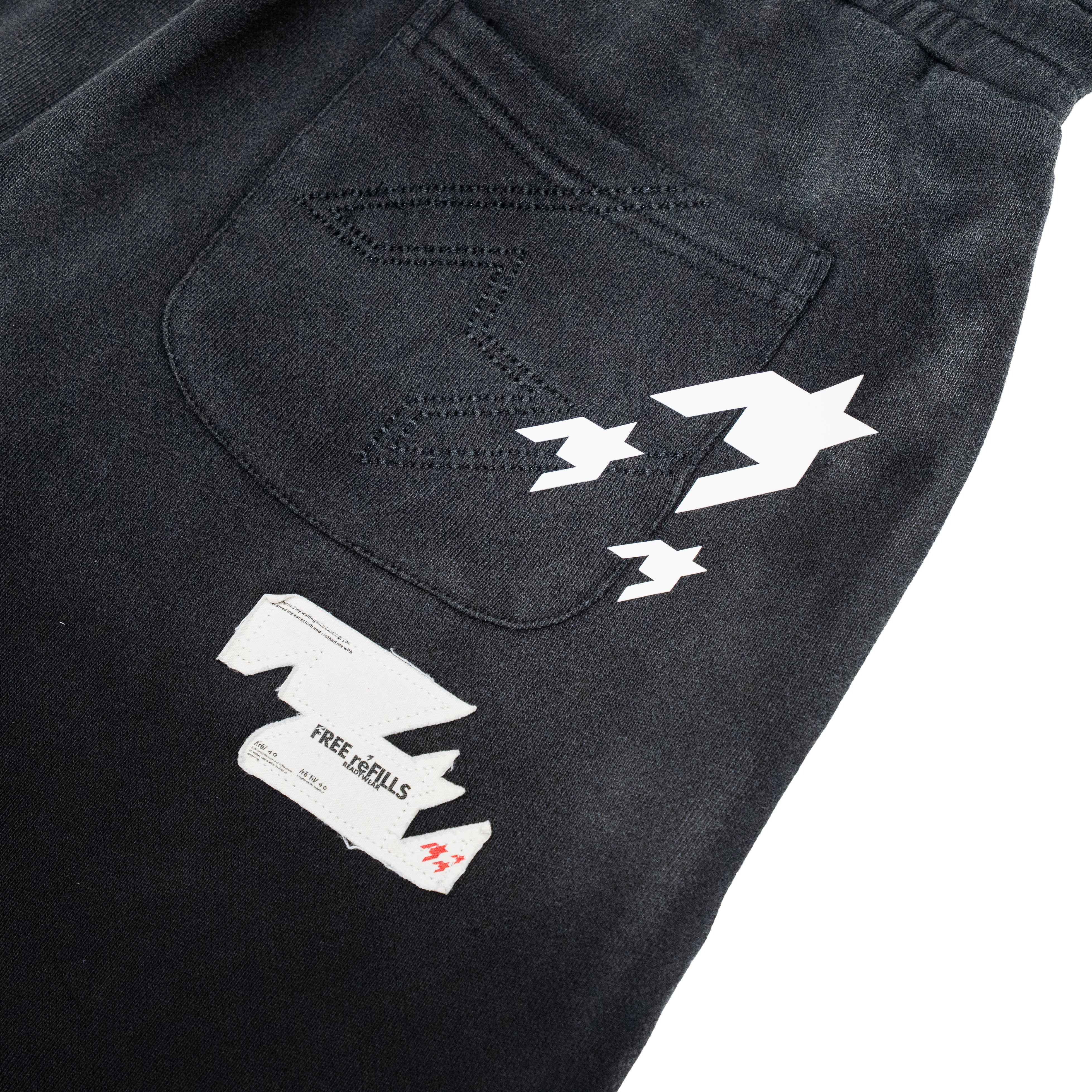Close-up of the back pocket of black denim jeans featuring a white graphic print and a white paper tag with the text 'FREE REFILLS'.