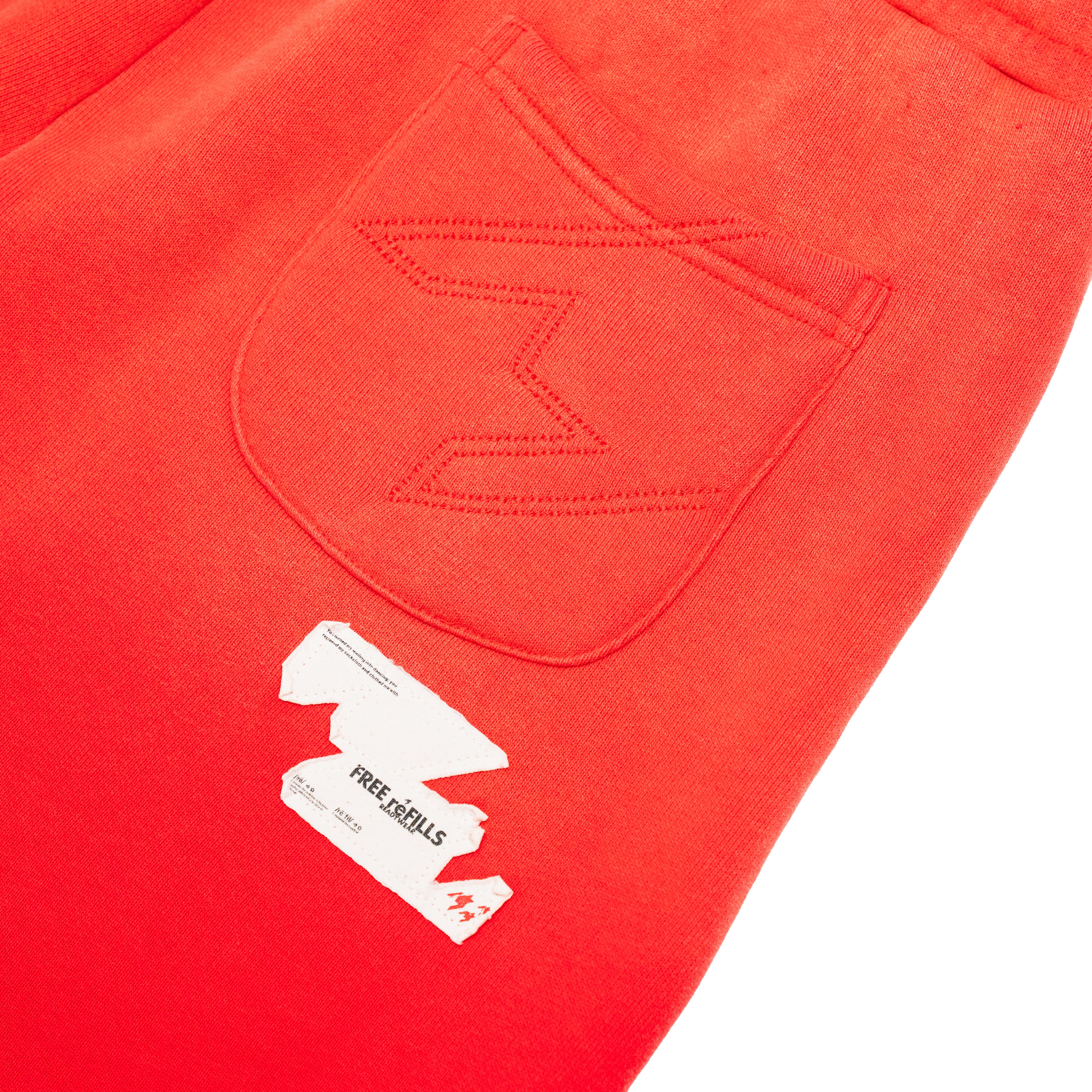 Close-up of bright red sweatpants showing a stitched back pocket and a white paper tag with the brand name Free REFILLS.