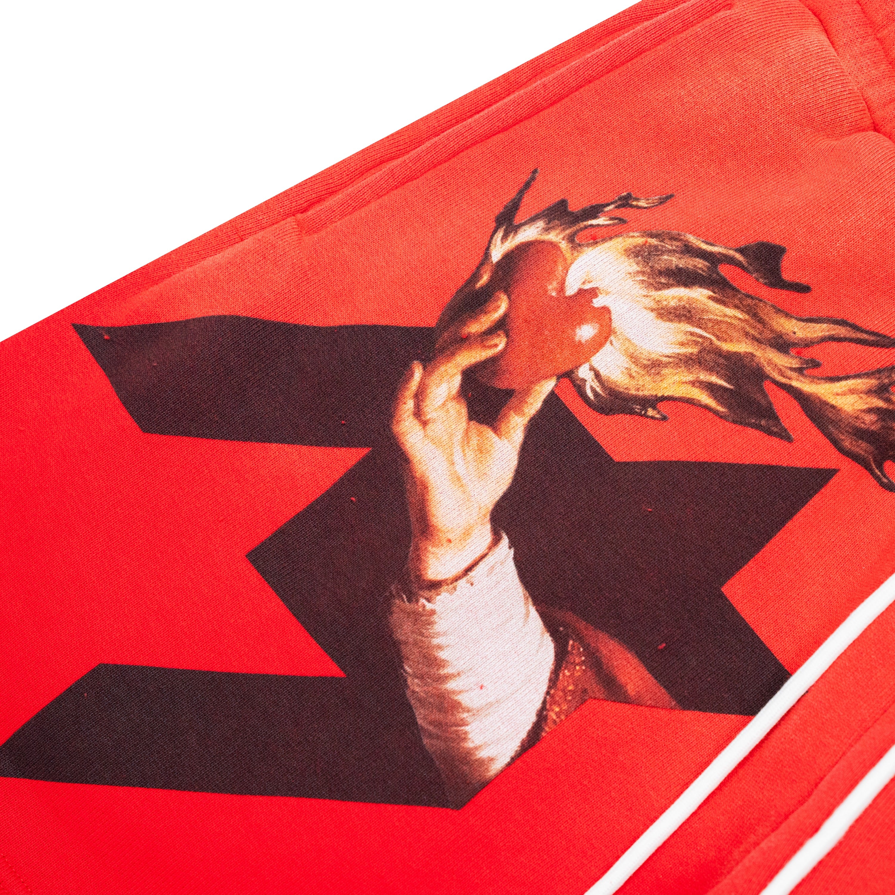 A close-up of a red shorts, featuring a graphic print of a hand holding a burning red heart over a black star shape.