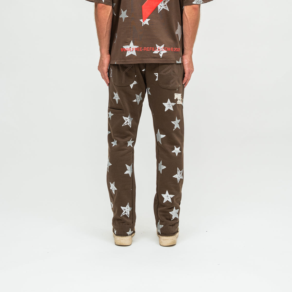 A person shown from the back wearing brown pants with a white star pattern and a matching brown shirt, photographed against a plain light gray studio background.