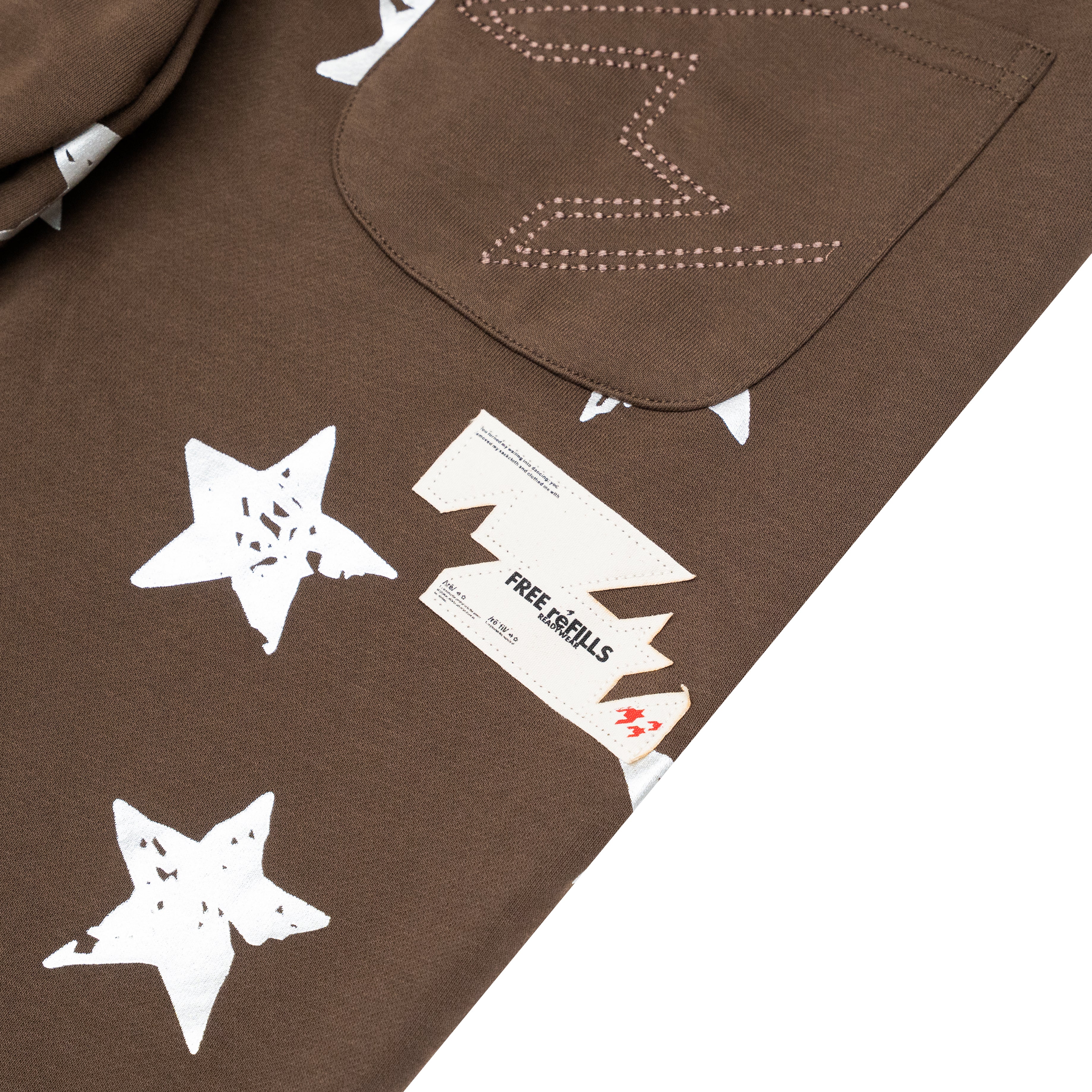 Close-up of a brown garment with white star graphics, a pocket with white stitched lightning-bolt detail, and a visible Free Refills brand tag.