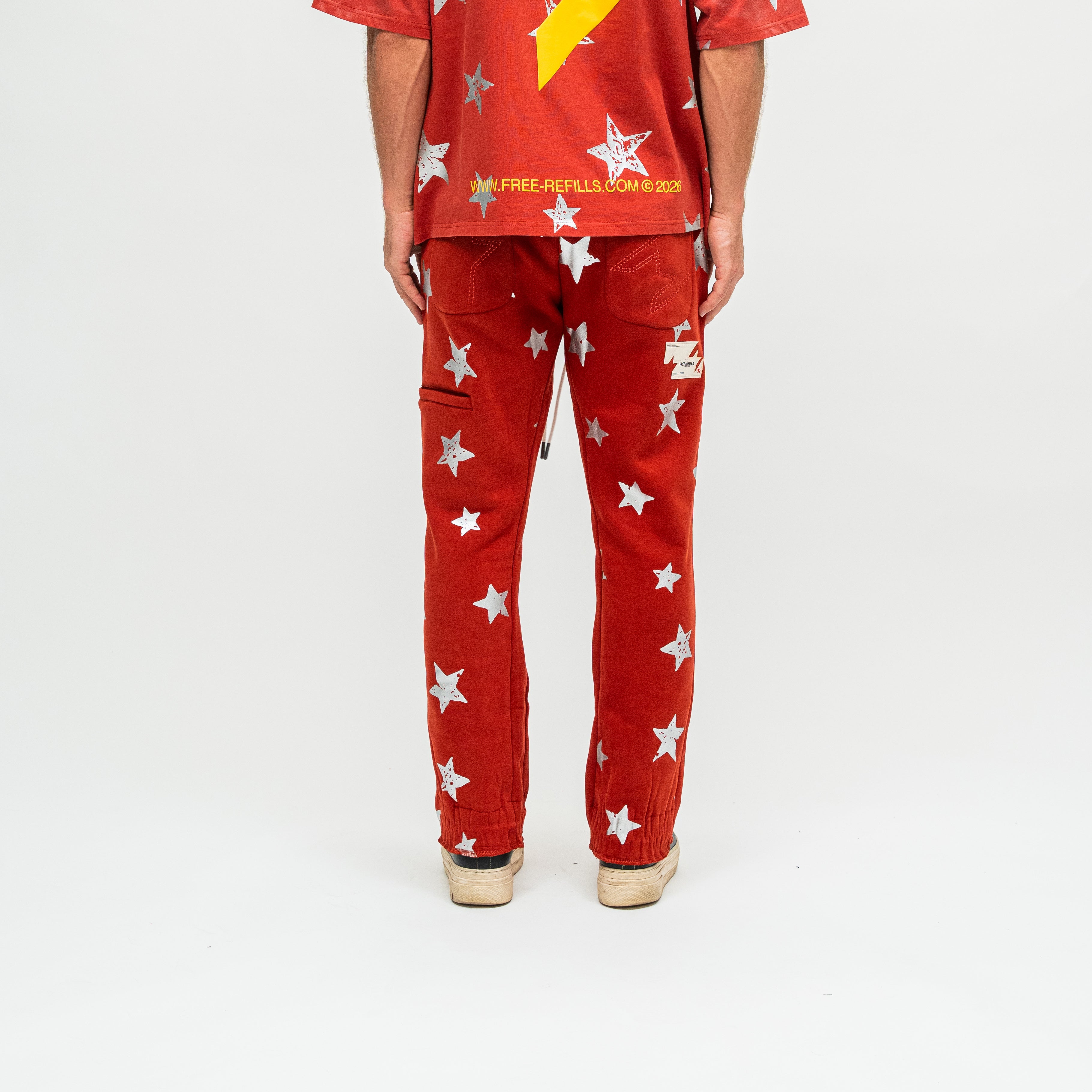 A person shown from the back wearing red pants with a white star print and a matching red shirt with a yellow star, photographed against a plain white studio background.